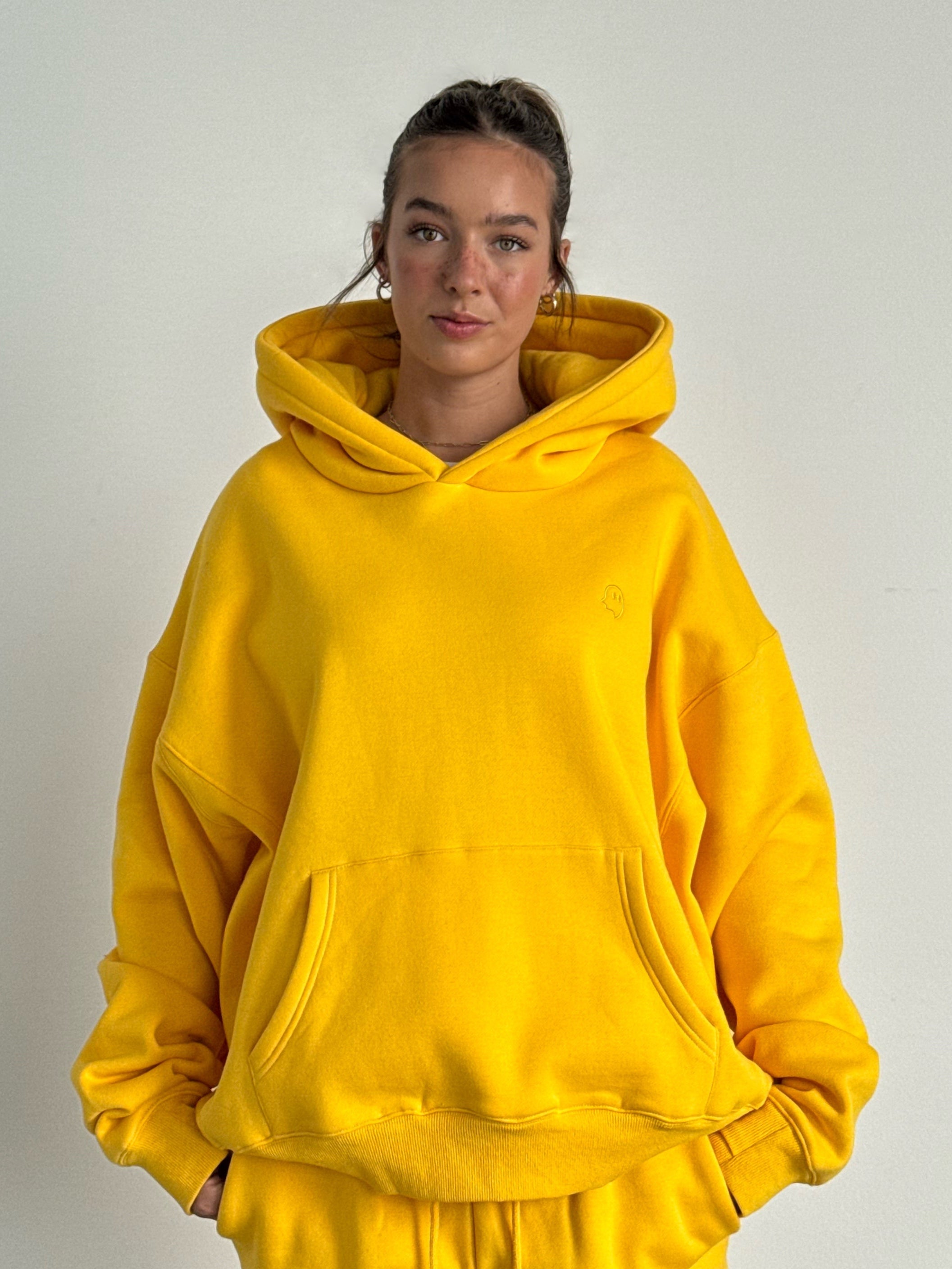 Person wearing a yellow hoodie and pants against a plain background