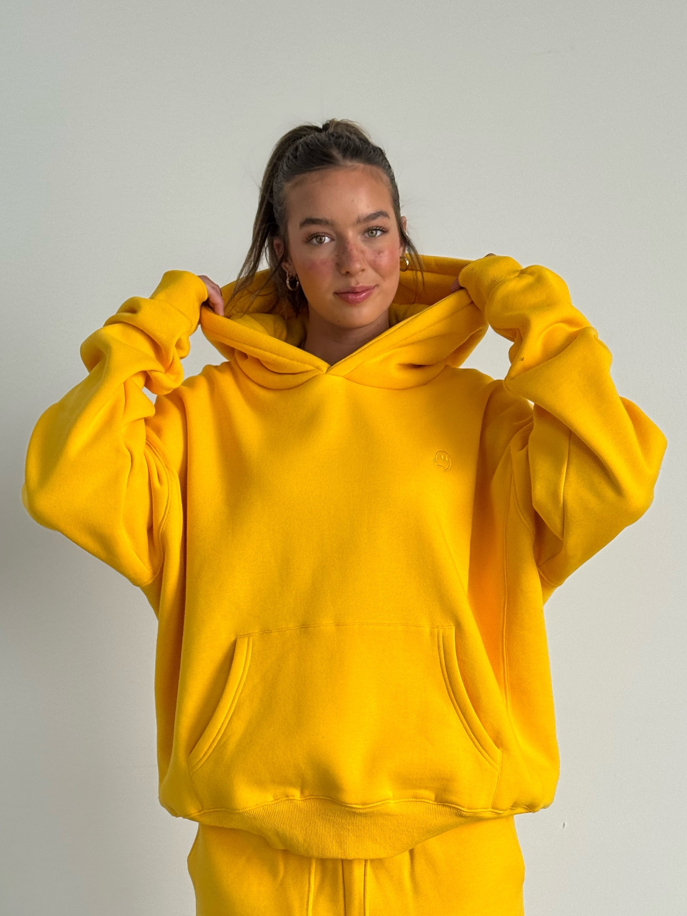 Person wearing a yellow hoodie and pants against a plain background