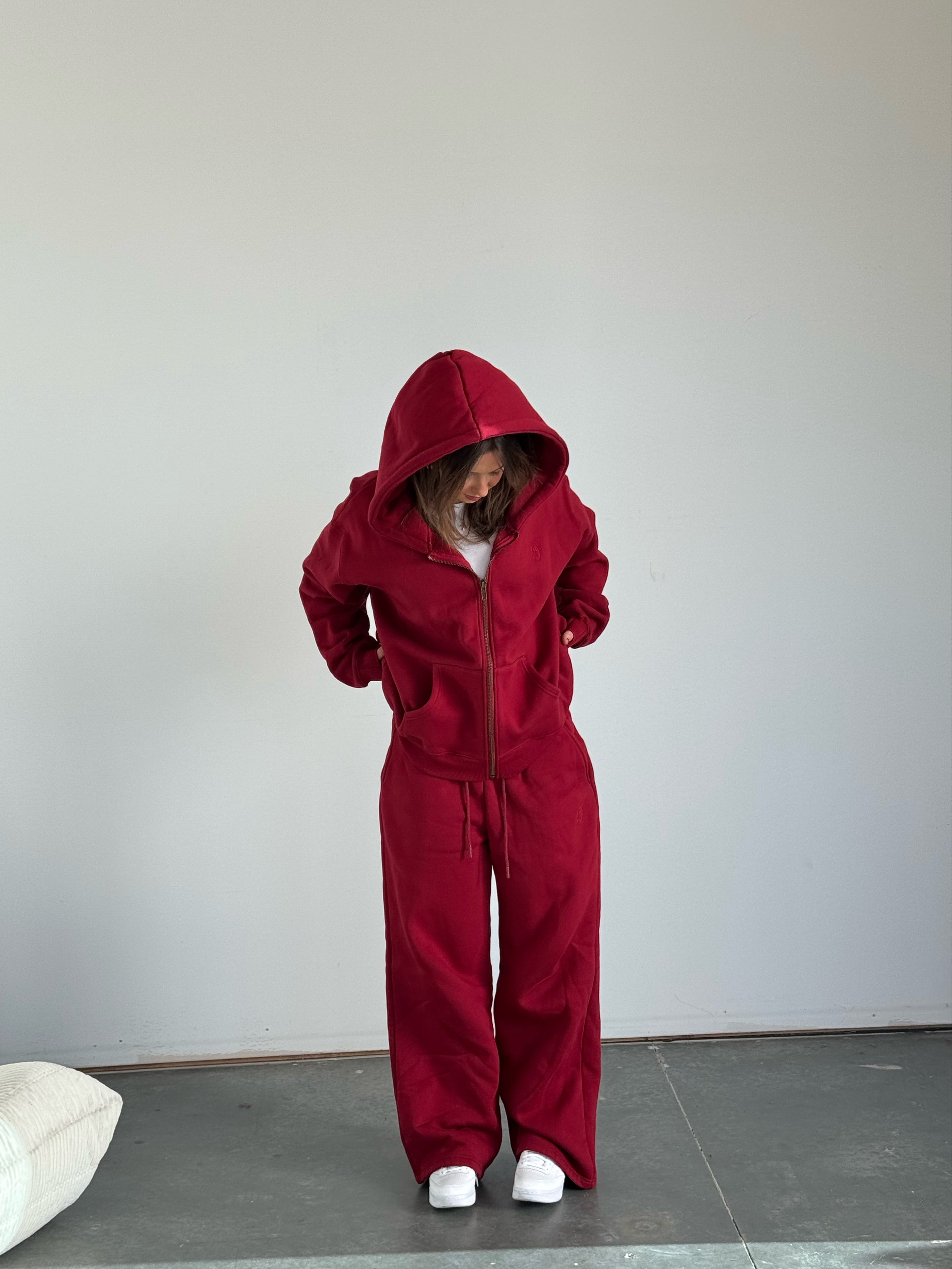 Person wearing a red hoodie and matching pants in a minimal indoor setting.