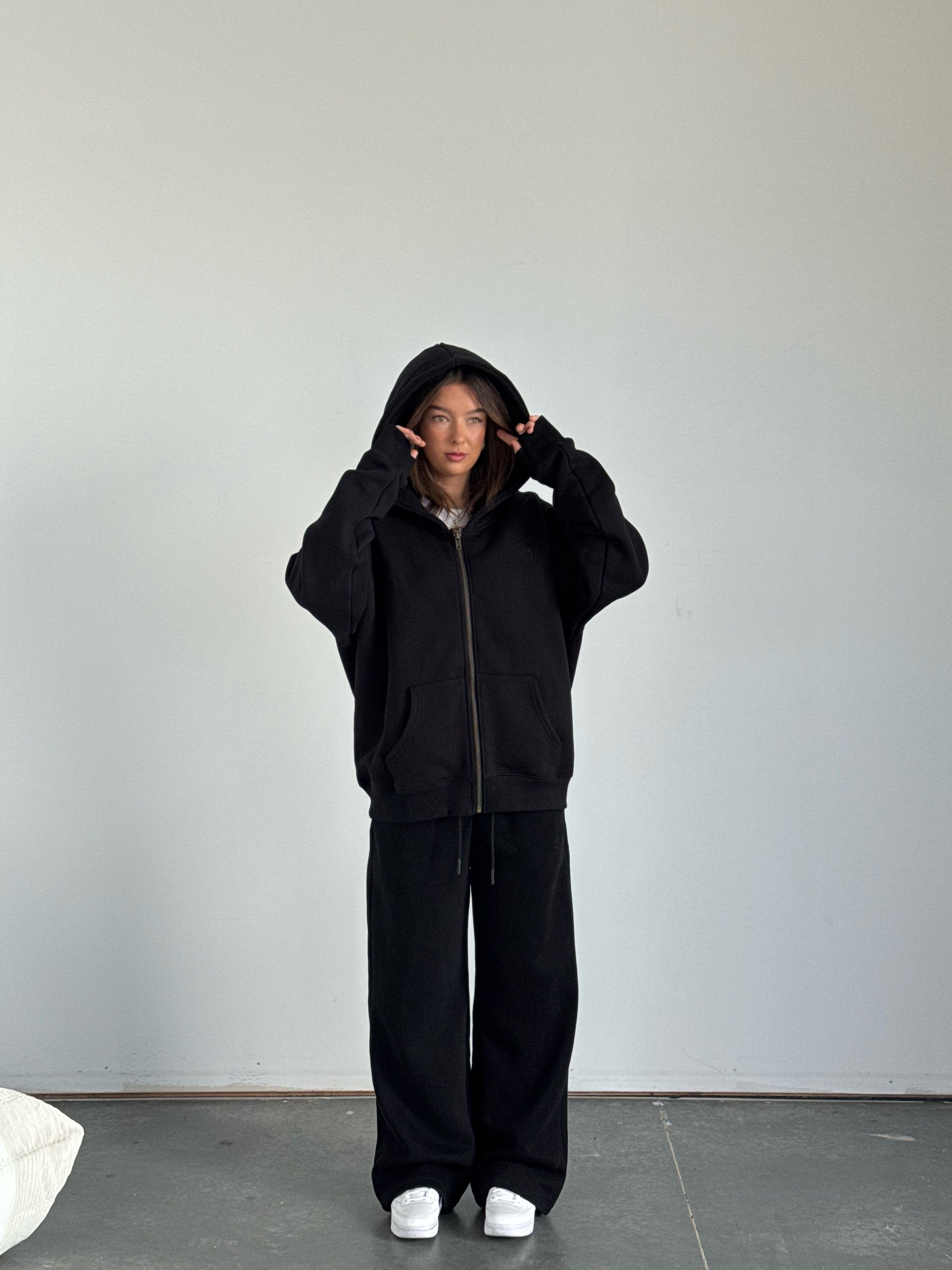 Person wearing a black hoodie and pants in a minimalistic setting