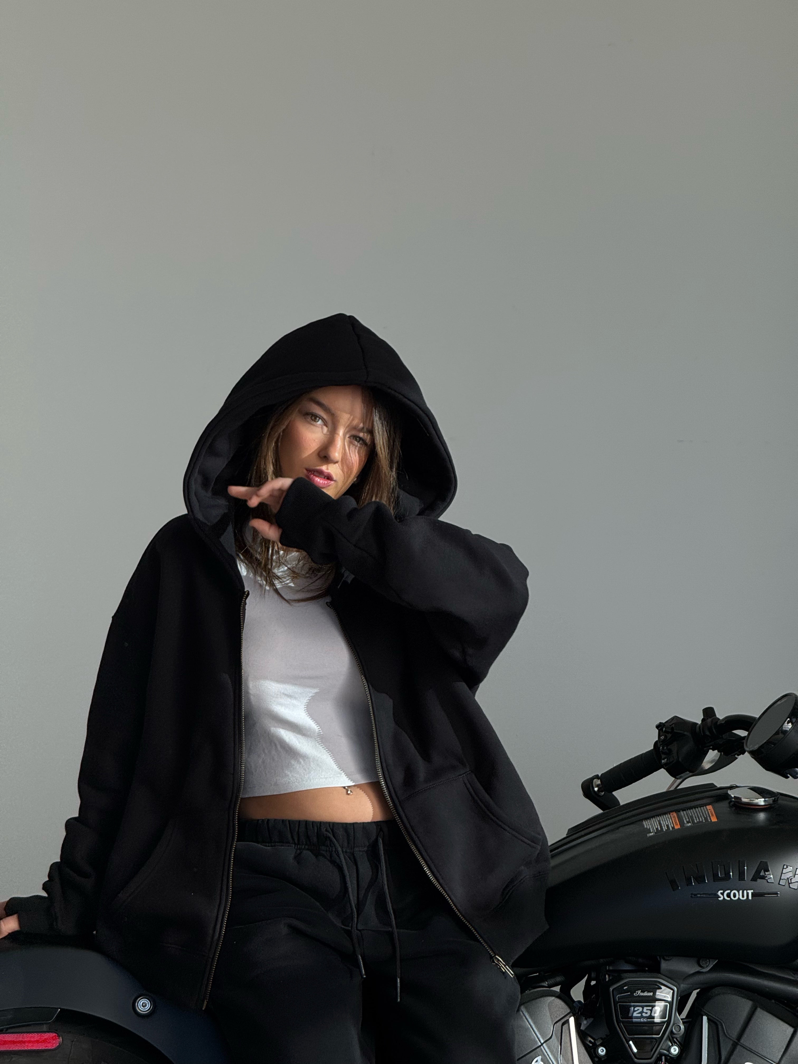 Person wearing a black hoodie sitting on a motorcycle with a gray background