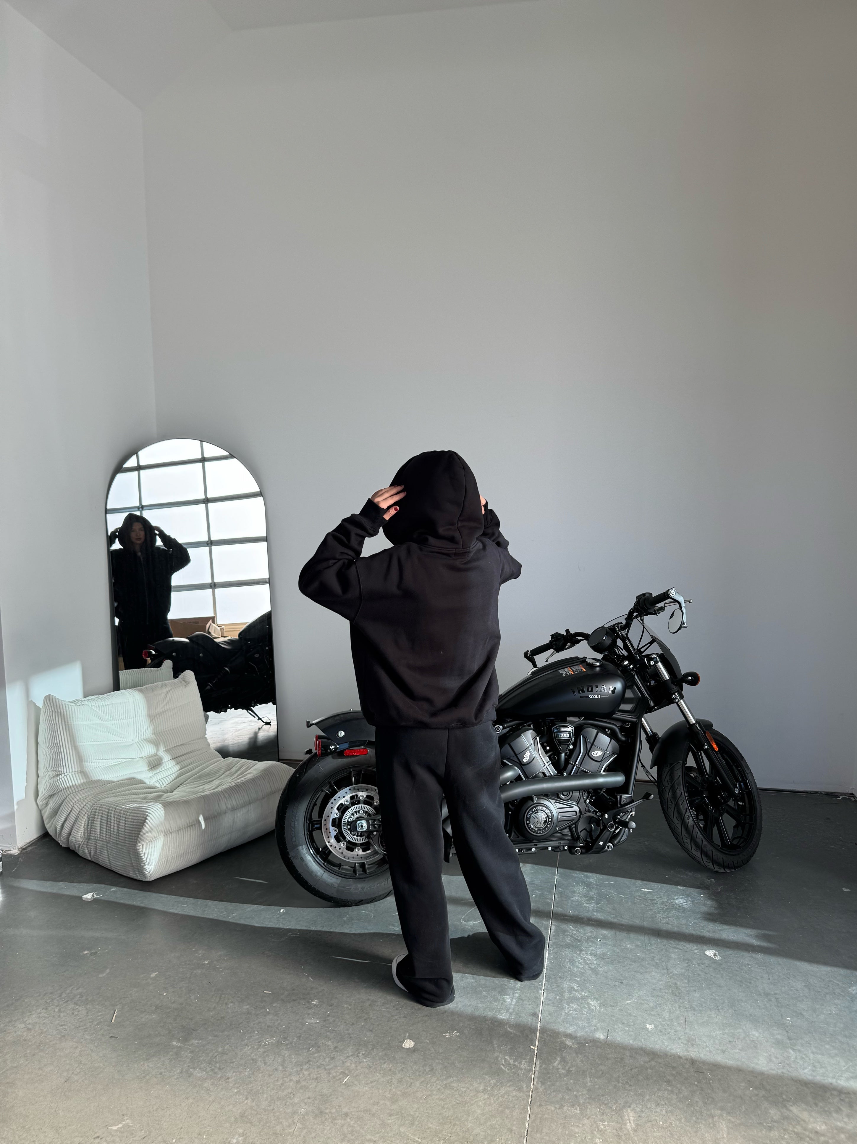Person standing in a room with a motorcycle and a couch, looking at themselves in the mirror.