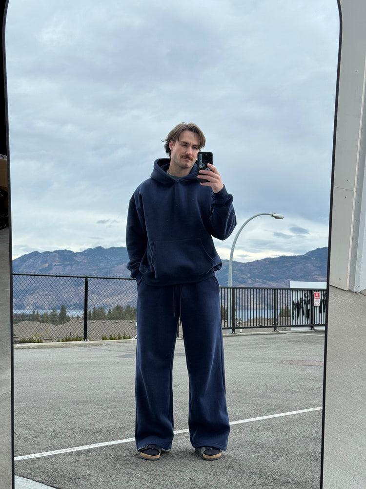 Person taking a mirror selfie wearing a navy blue hoodie and pants with mountains in the background.