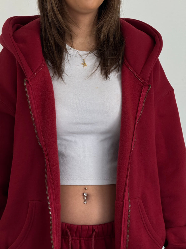 Person wearing a red hoodie over a white top and red pants on a plain background