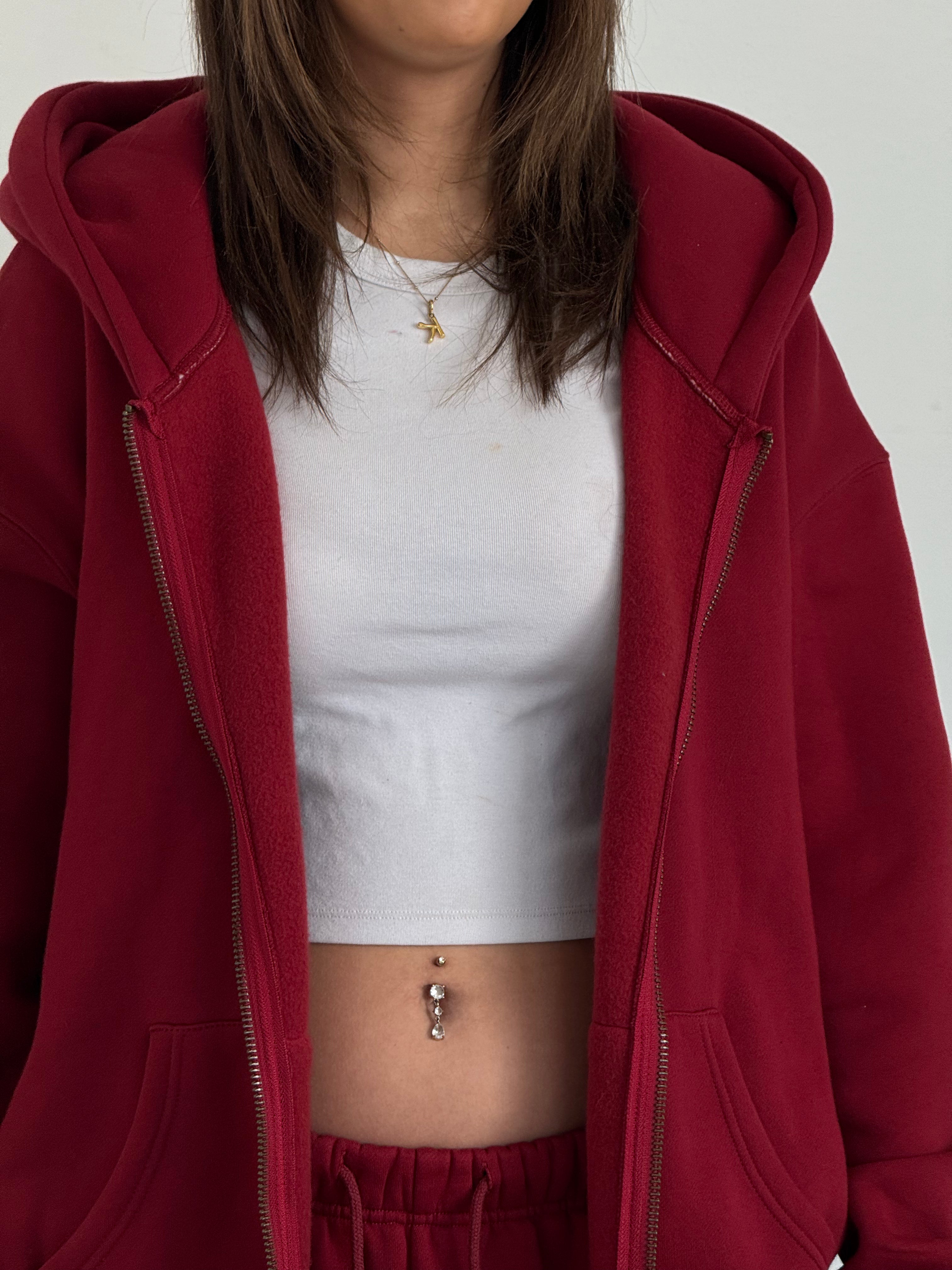 Person wearing a red hoodie over a white top and red pants on a plain background