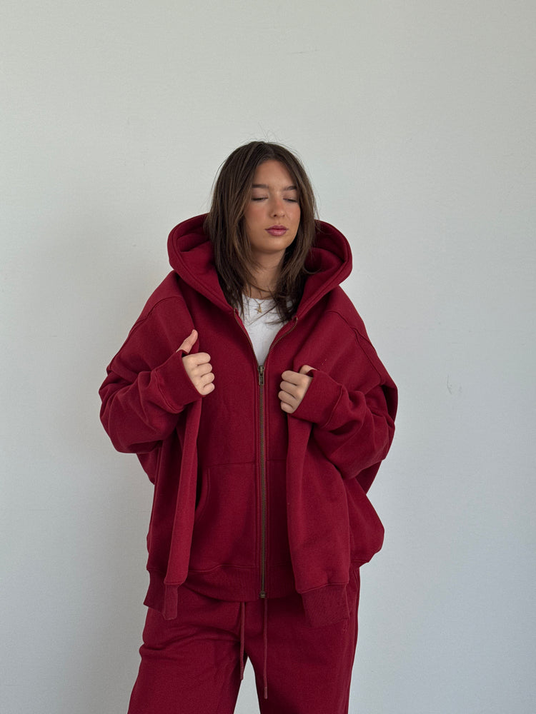 Person wearing a red hoodie and pants against a plain background