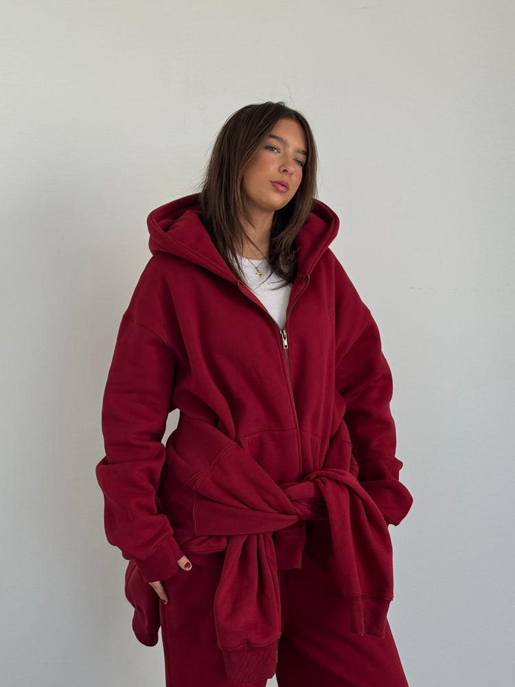 Person wearing a red hoodie and pants against a plain background