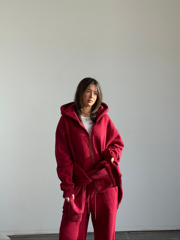 Person wearing a red tracksuit standing against a plain white wall.