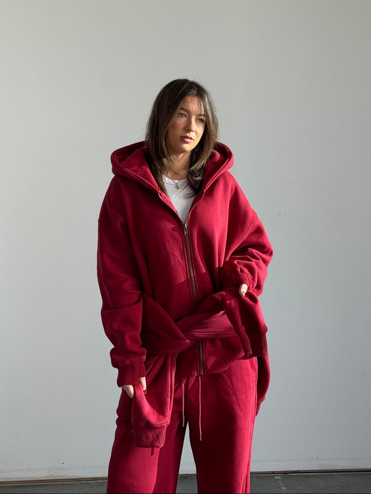 Person wearing a red tracksuit standing against a plain white wall.