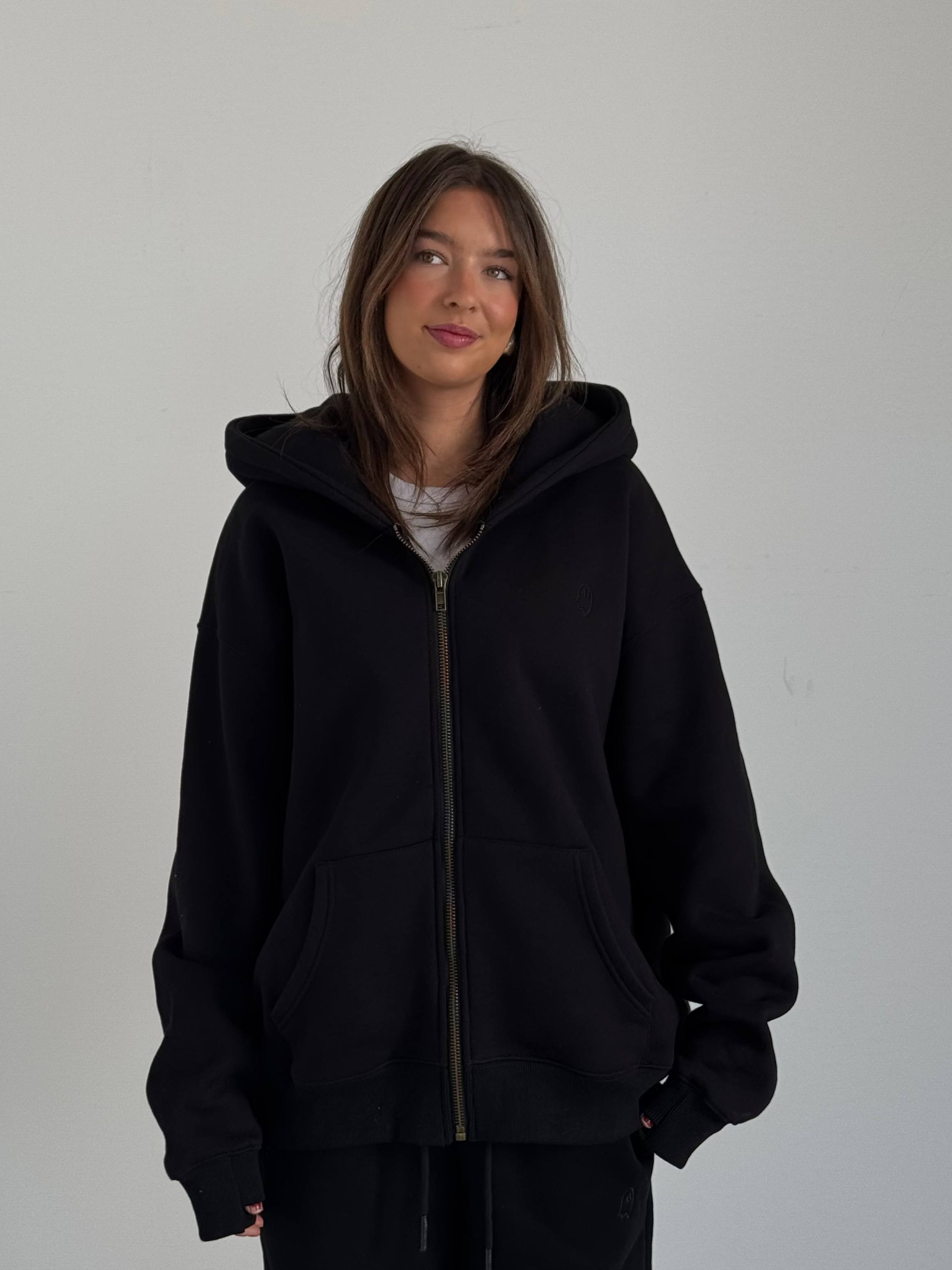 Person wearing a black hoodie and pants against a plain background