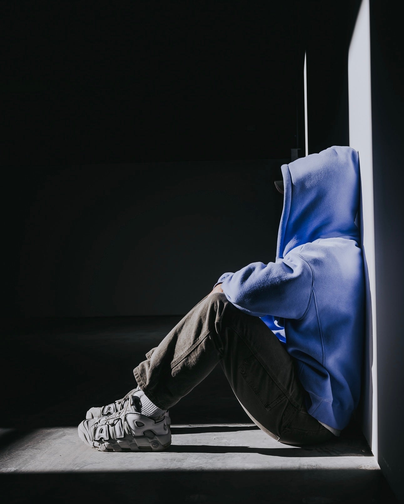 Person wearing a blue hoodie sitting in a dark corner