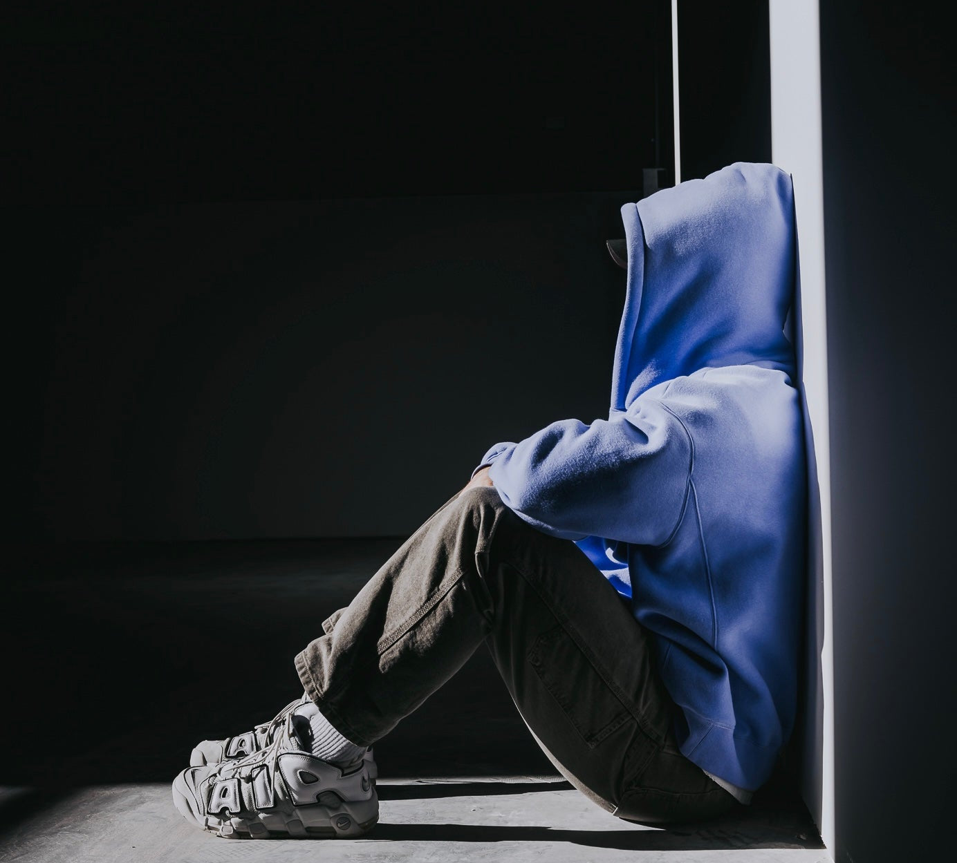 Person wearing a blue hoodie sitting in a dark corner
