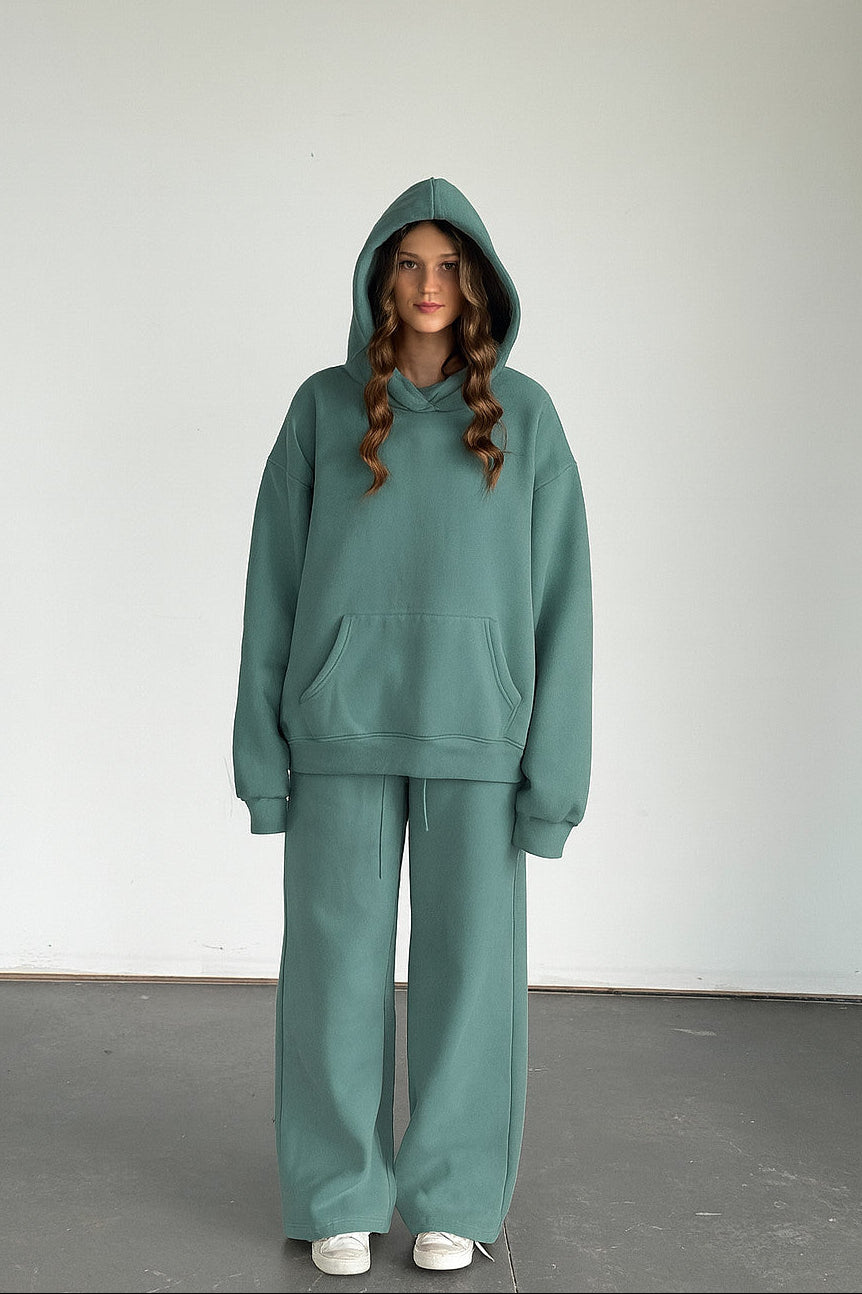 Person wearing a teal hoodie and pants set against a plain background