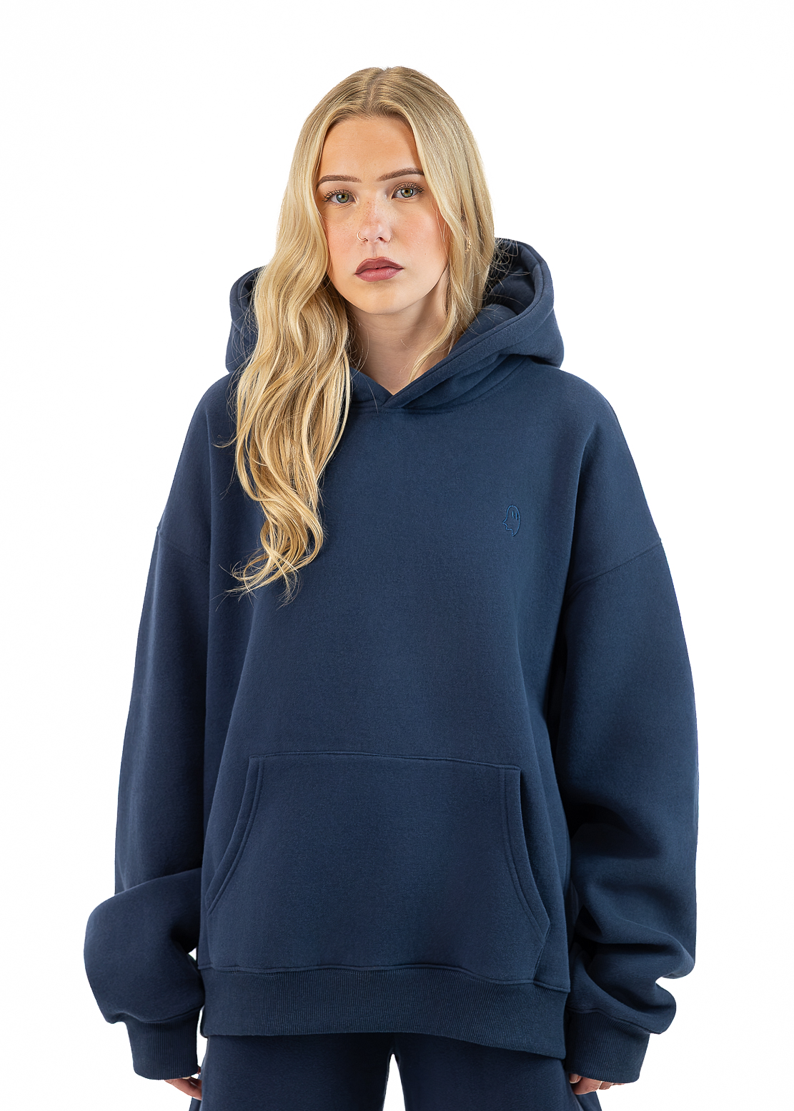 A blonde woman wearing an oversized navy blue pullover hoodie with a front kangaroo pocket, paired with matching navy pants, photographed against a solid white background.