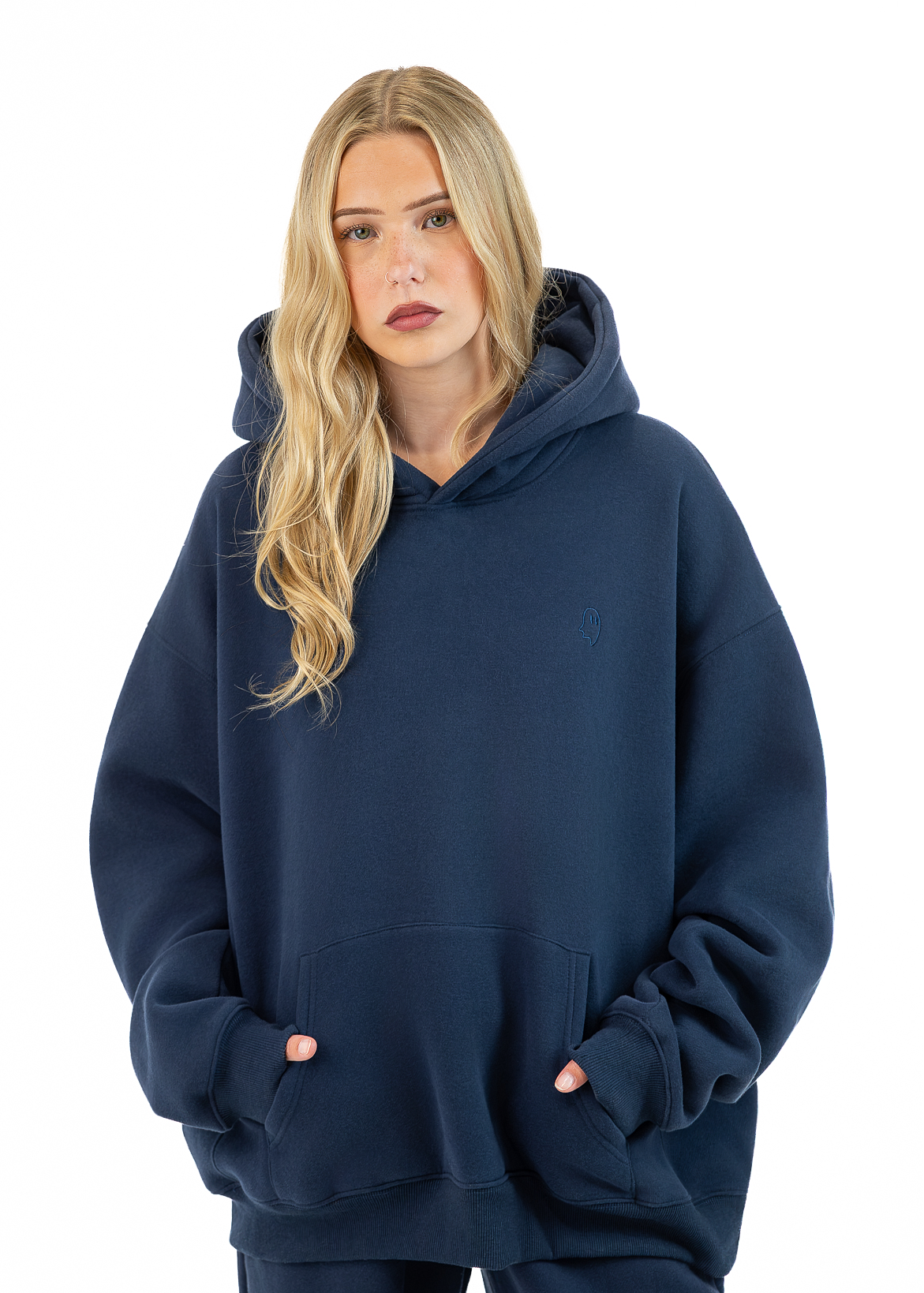 A blonde woman wearing an oversized navy blue pullover hoodie with a front kangaroo pocket, posed against a solid white background.