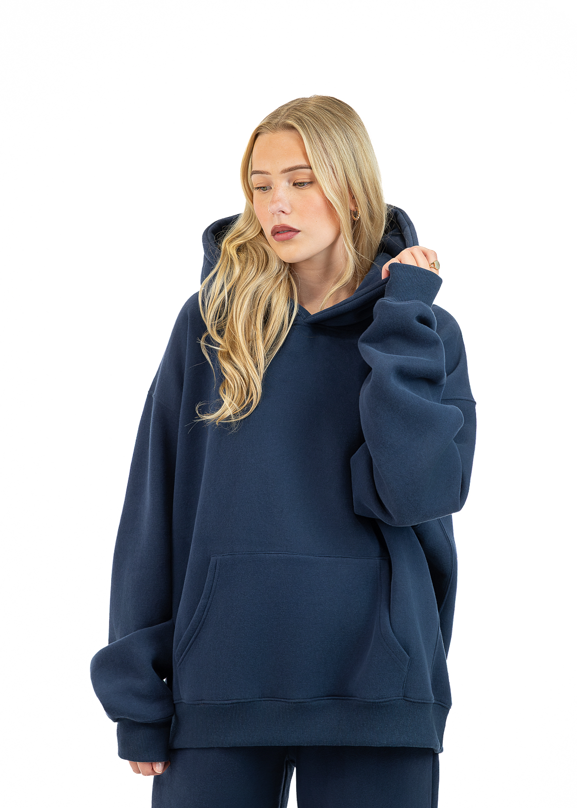 A woman wearing an oversized navy blue hoodie and matching sweatpants, standing against a plain white studio background.