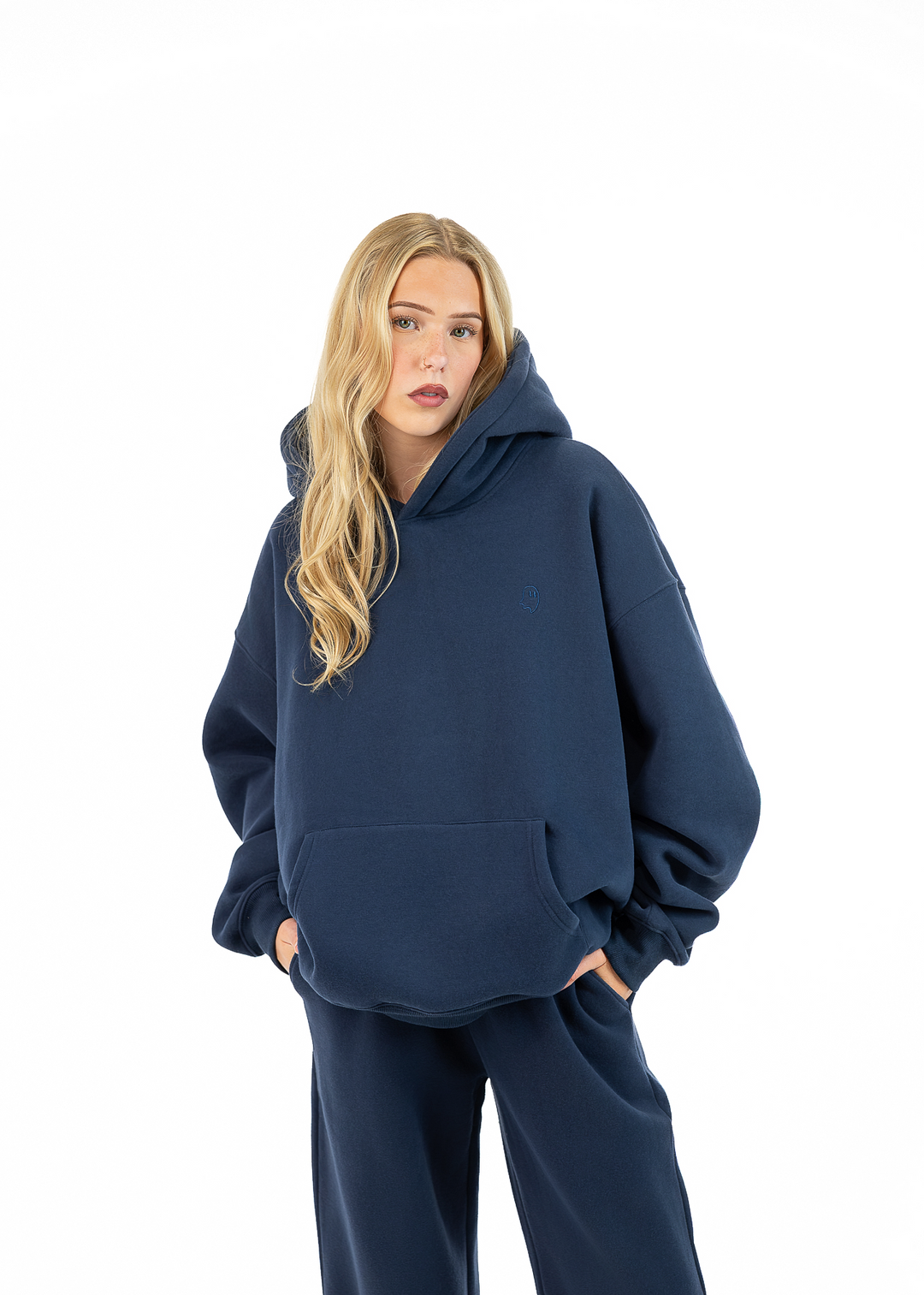 A woman modeling an oversized navy blue hoodie and matching sweatpants against a plain white background.