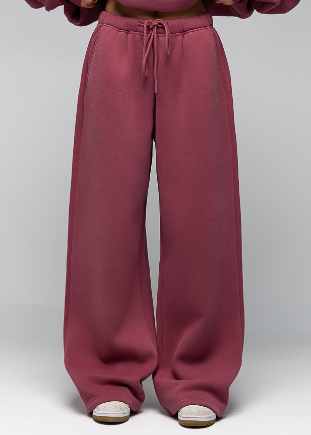A model wearing a matching dusty rose sweatshirt and wide-leg sweatpants, standing against a light gray studio background.