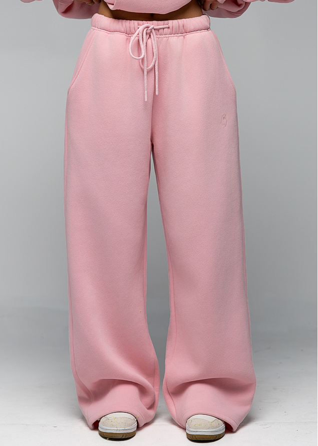 A person wearing light pink wide-leg sweatpants with a matching sweatshirt, shown from the chest down against a light gray studio background.