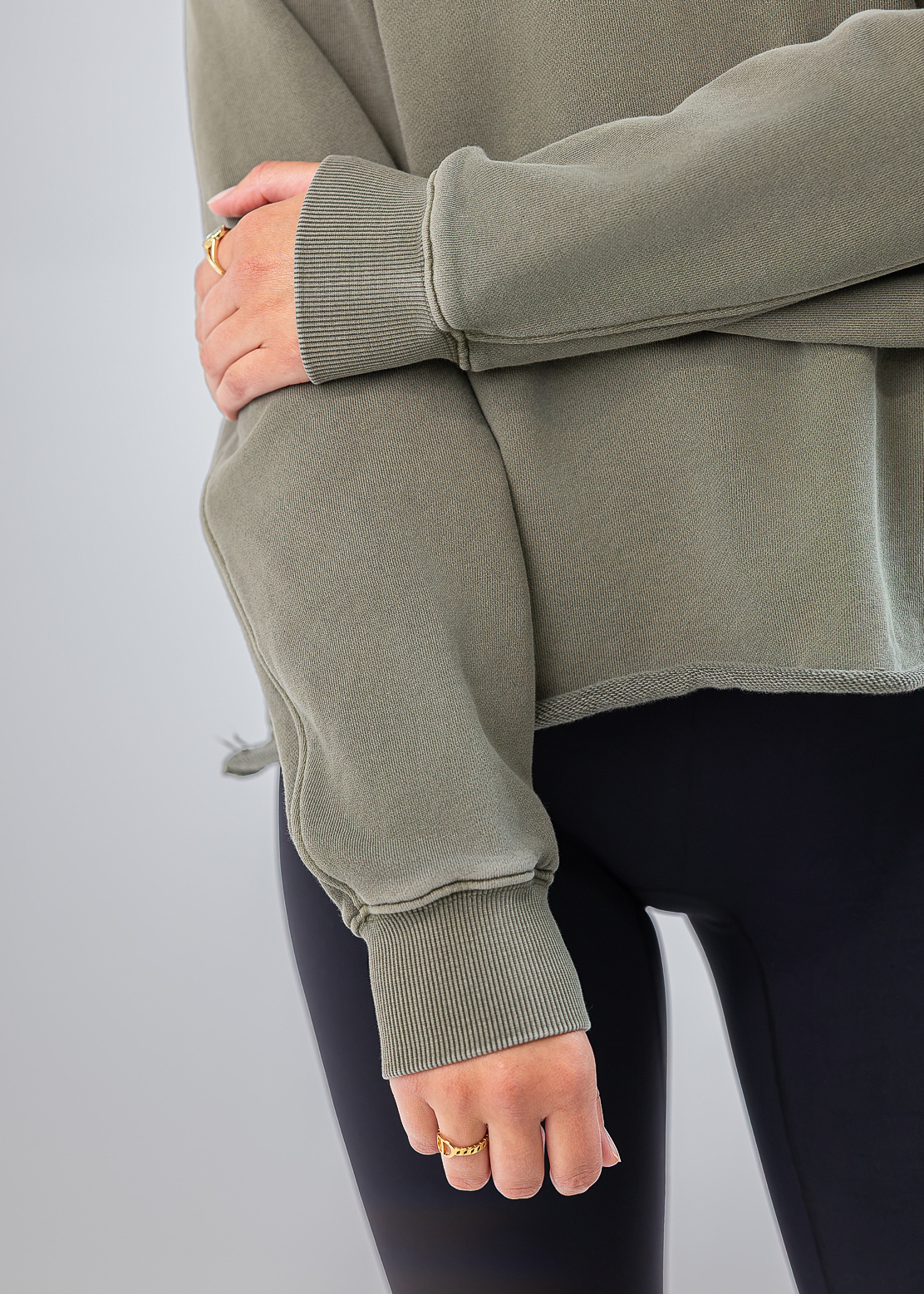 A close-up of a person wearing an oversized sage green sweatshirt and black leggings, with the focus on the ribbed cuffs and the fit of the garment.