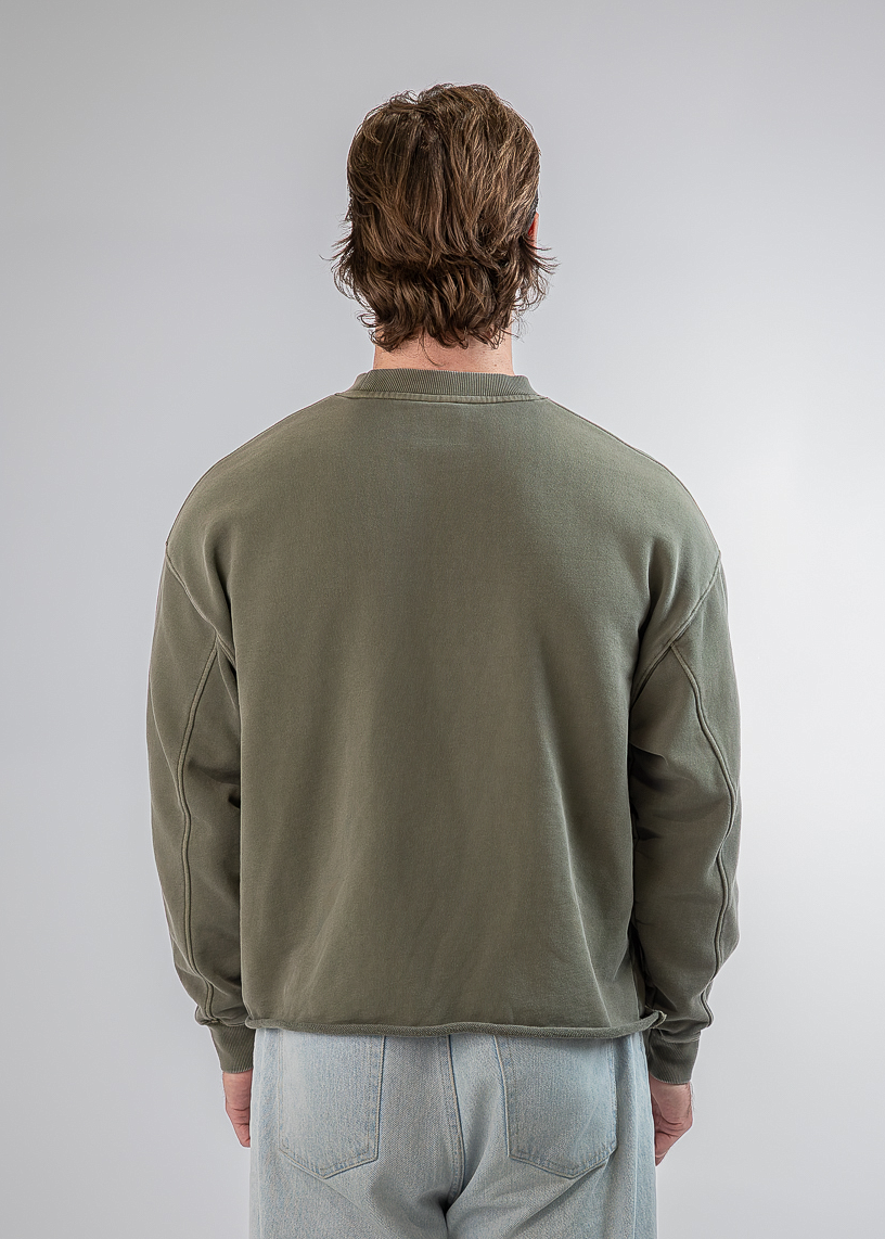A man viewed from behind wearing an olive green crewneck sweatshirt and light gray sweatpants, standing against a light gray studio background.