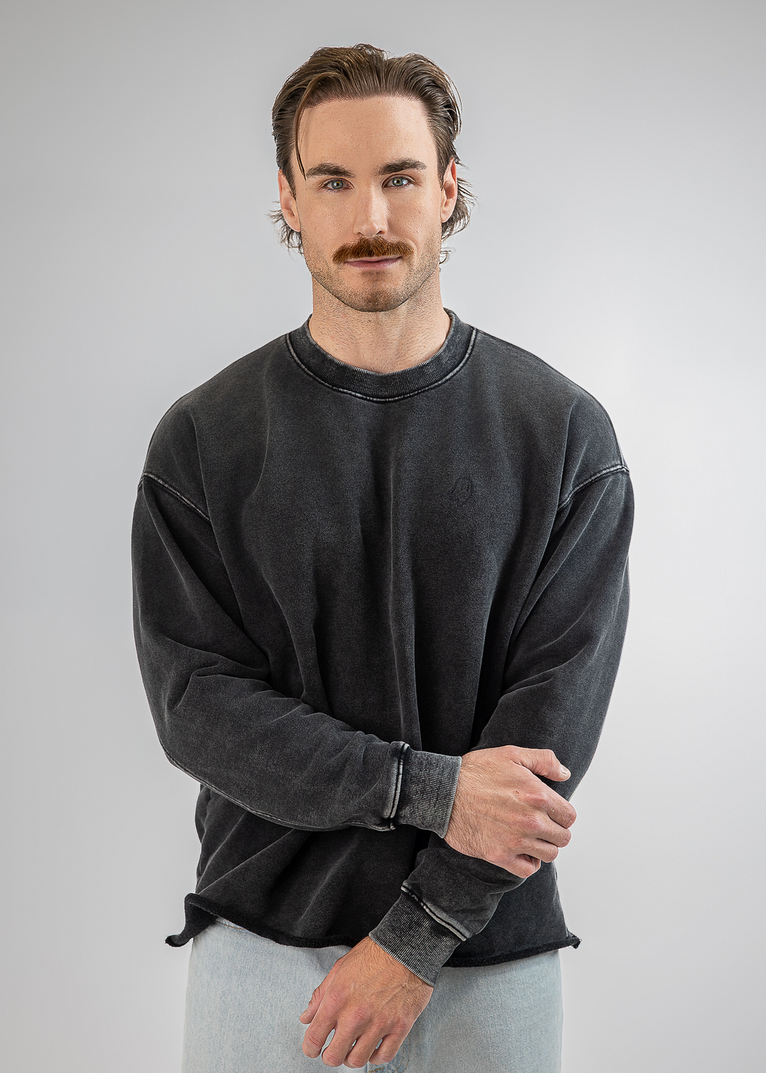 A man modeling a dark gray washed crewneck sweatshirt and light gray sweatpants against a neutral gray background.