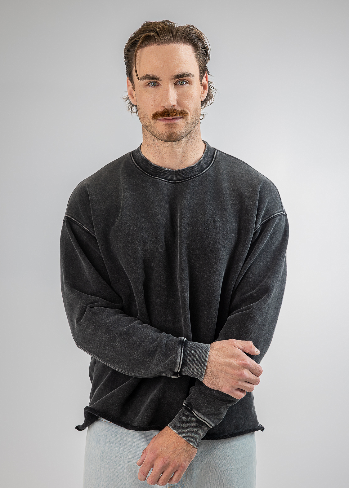 A man modeling a dark gray washed crewneck sweatshirt and light gray sweatpants against a neutral gray background.