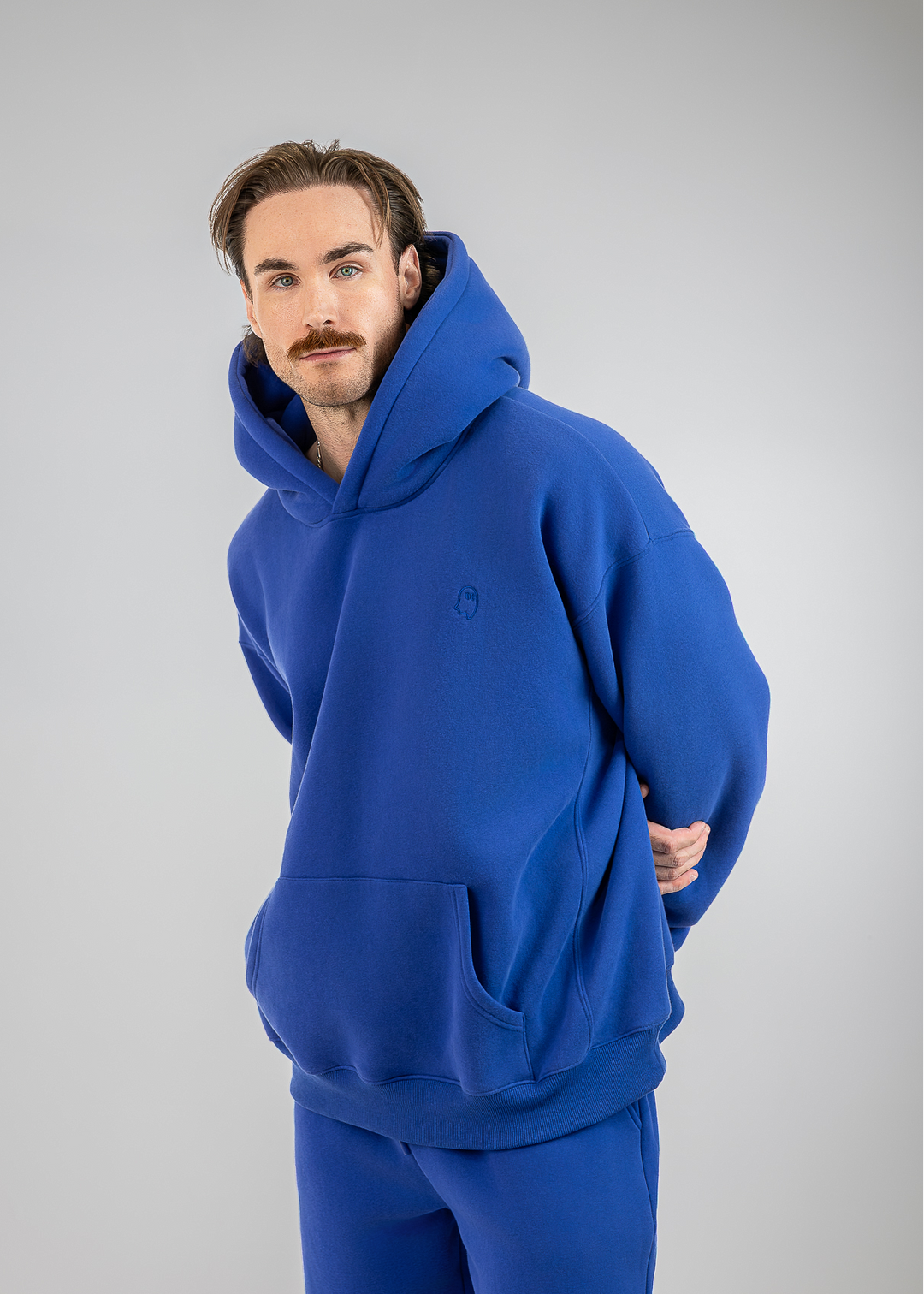 A man wearing a matching royal blue hoodie and sweatpants set, photographed against a neutral light gray studio background.