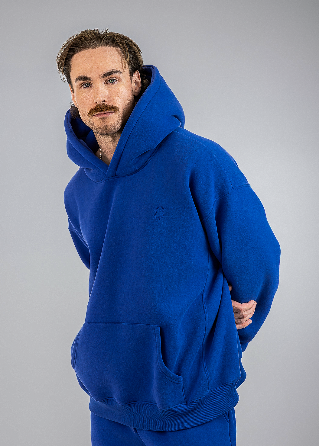A man wearing a vibrant royal blue hoodie and matching sweatpants, photographed against a neutral gray studio background.