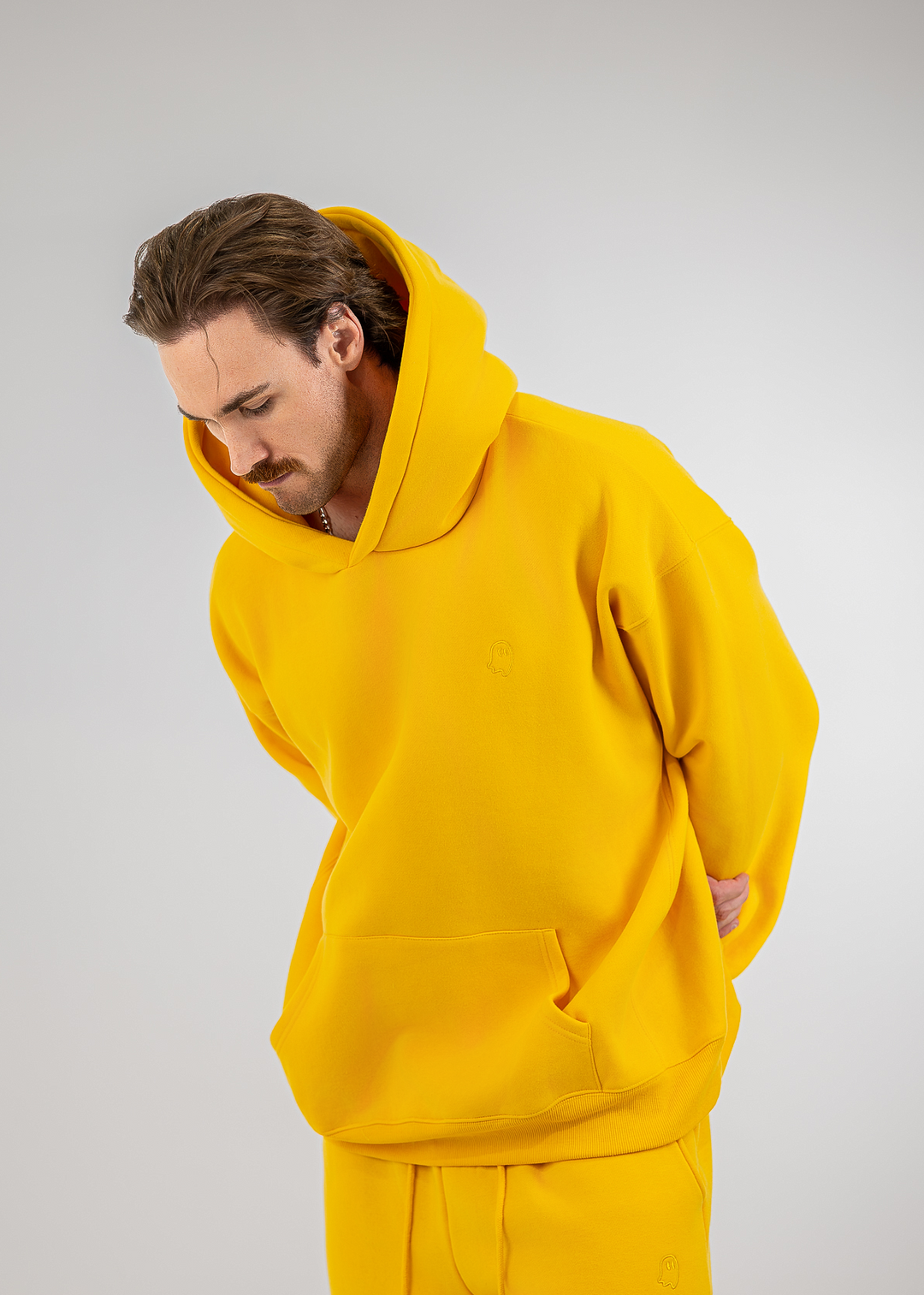 A man wearing a bright yellow hooded sweatshirt and matching sweatpants, photographed against a plain light gray studio background.