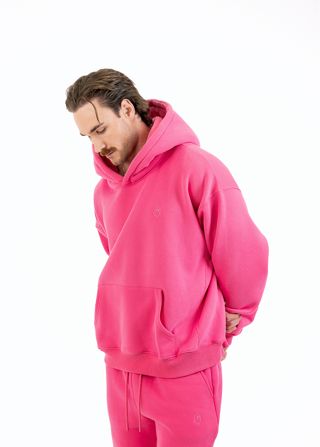 A man wearing a bright pink matching hoodie and sweatpants set, photographed against a clean white studio background.