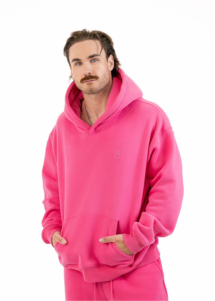 A man wearing a bright pink matching hoodie and sweatpants set, standing against a plain white background.
