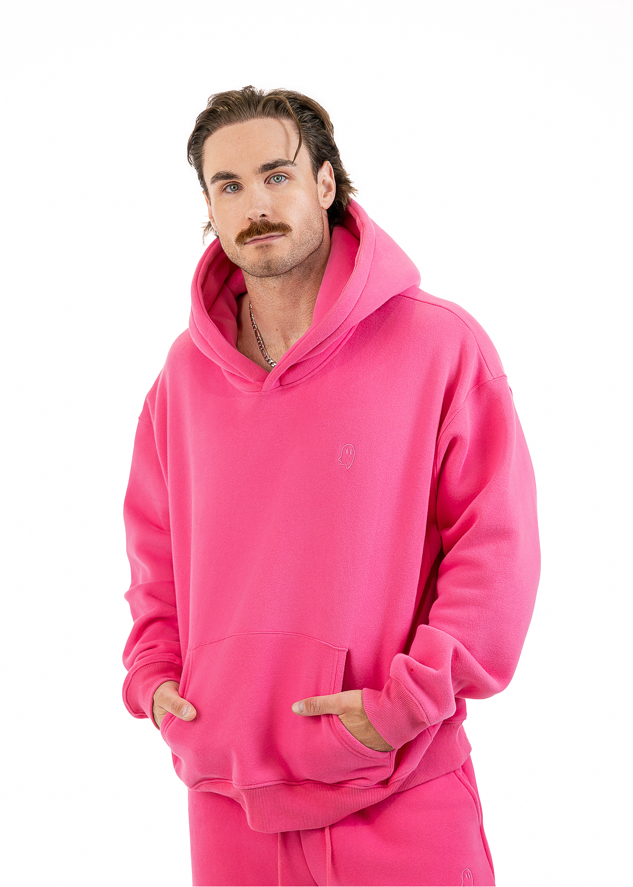 A man wearing a bright pink matching hoodie and sweatpants set, standing against a plain white background.