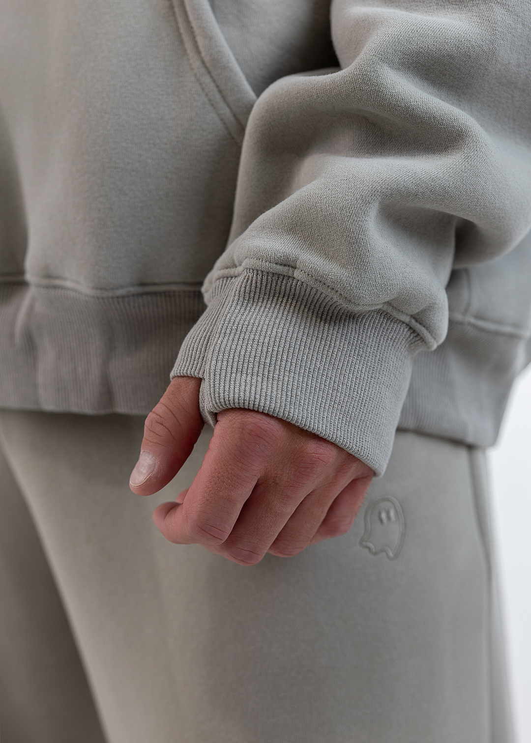 Close-up of a person wearing a light gray ribbed sweatshirt and matching sweatpants, with the hand resting near the pocket area.