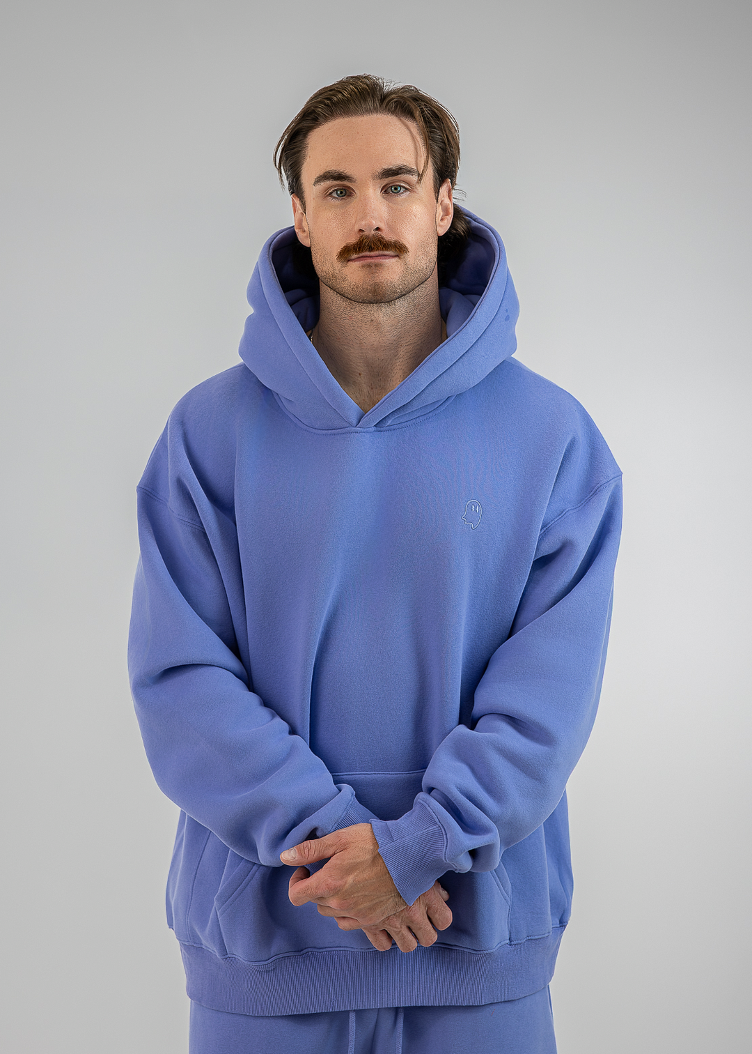 A man wearing a matching blue hoodie and sweatpants set, standing against a neutral gray studio background.