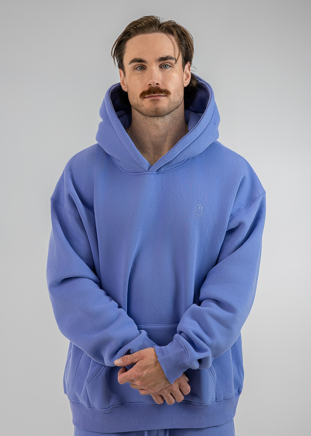 A man wearing a matching blue hoodie and sweatpants set, standing against a neutral gray studio background.
