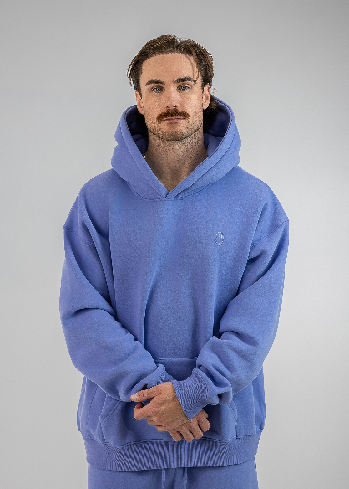 A man wearing a matching blue hoodie and sweatpants set, standing against a neutral gray studio background.