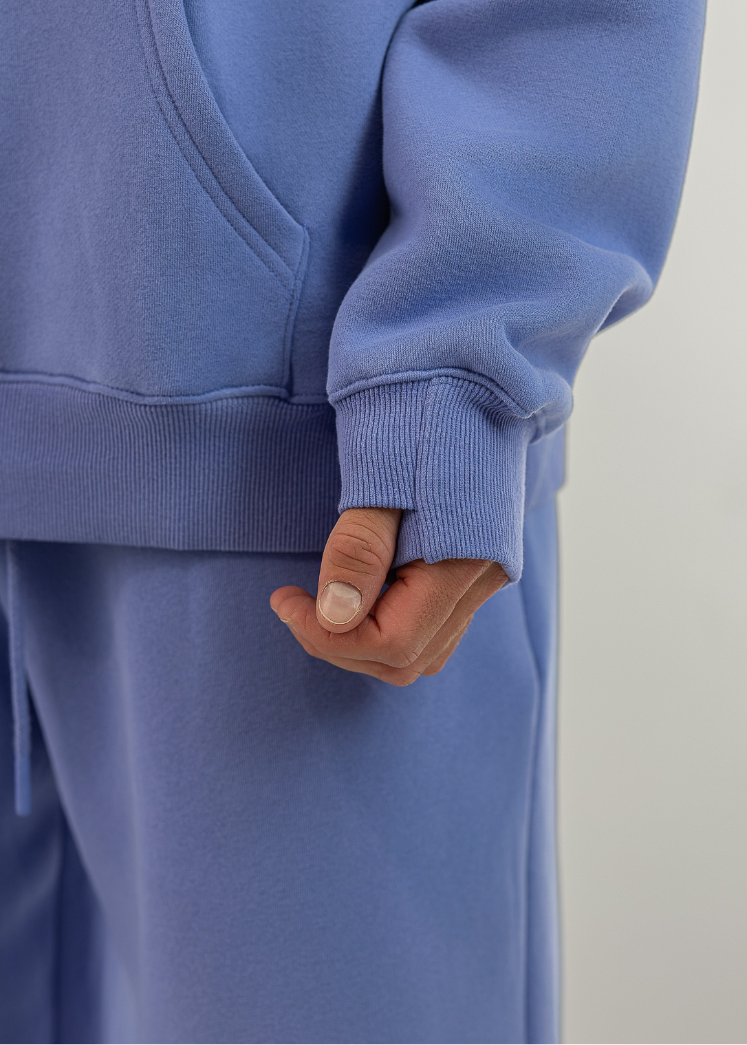 A close-up of a person wearing a matching dusty blue sweatshirt and sweatpants set, showing the ribbed cuffs of the hoodie and the fabric of the pants.