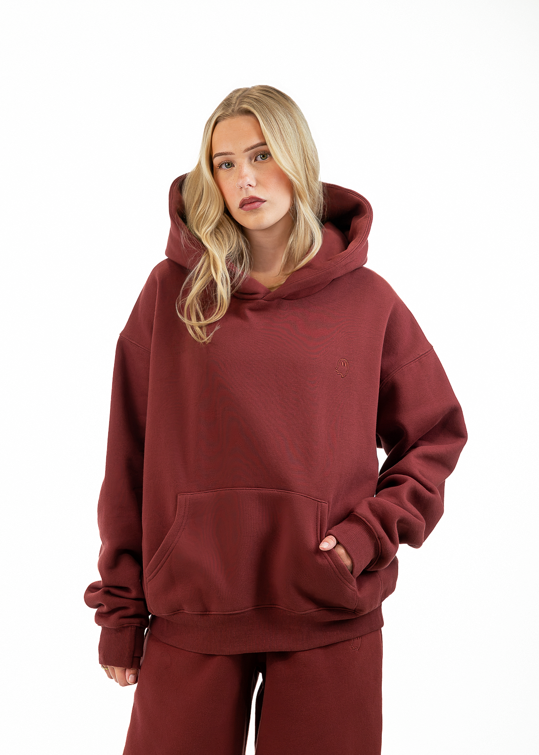 A blonde woman wearing a matching burgundy hoodie and sweatpants set, standing against a plain white studio background.