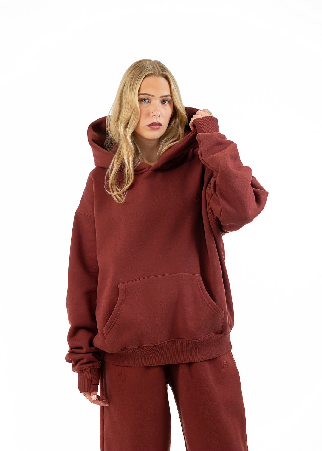 A woman modeling a matching rust-brown hoodie and sweatpants set against a plain white background.