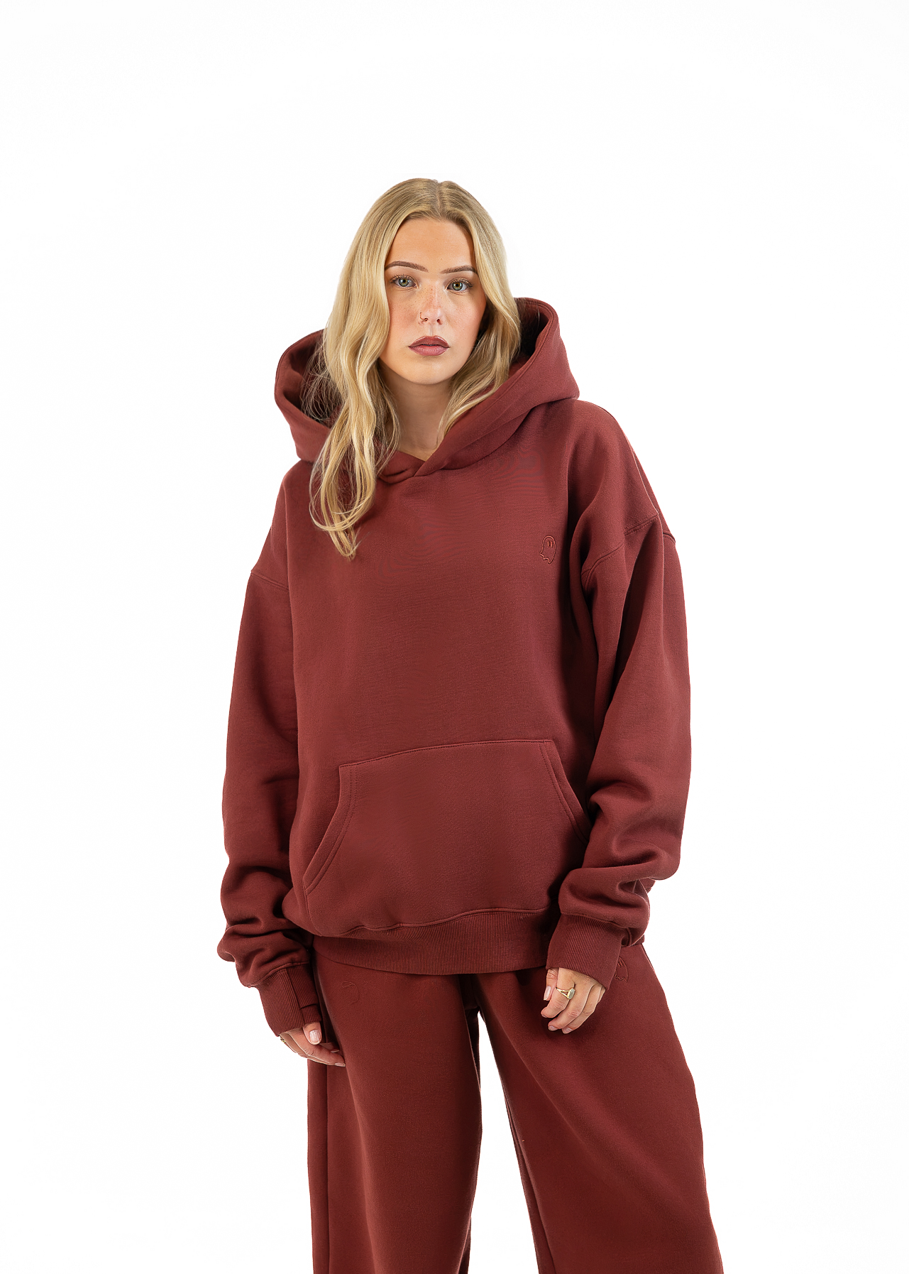 A woman modeling an oversized rust-brown hooded sweatshirt and matching wide-leg sweatpants against a plain white background.