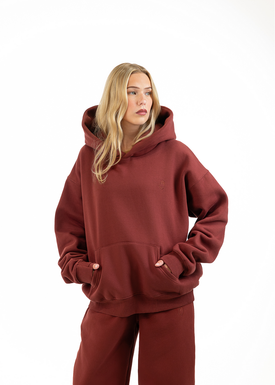 A woman modeling an oversized rust-brown hoodie and matching sweatpants against a plain white studio background.