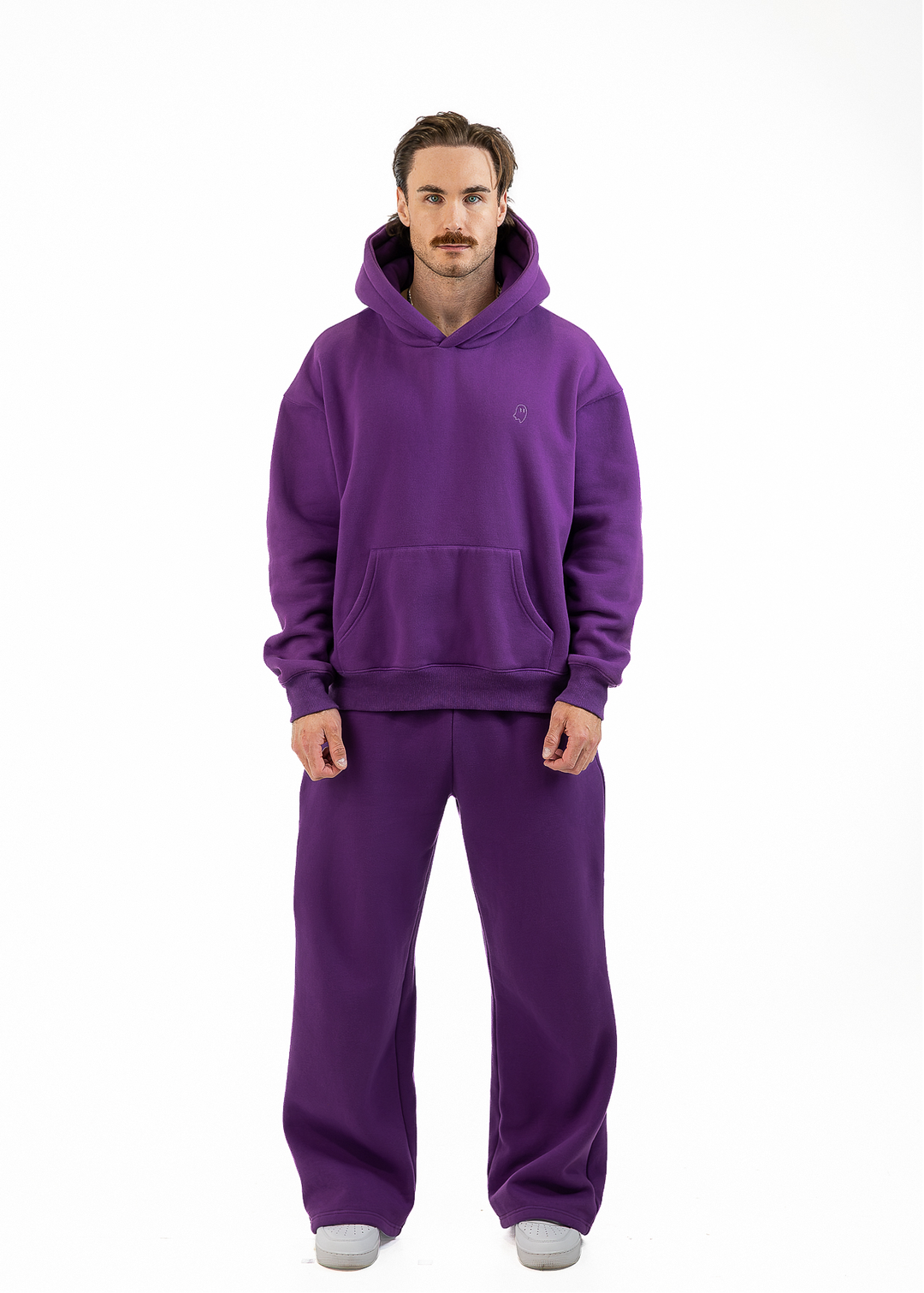 A man wearing a matching purple hoodie and sweatpants set, standing against a plain white background.