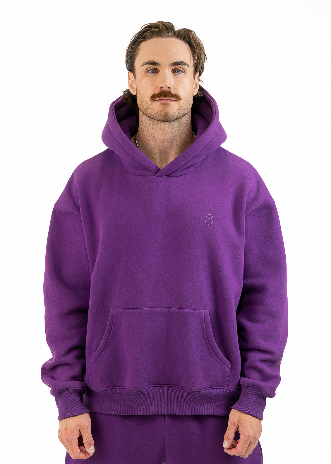 A man wearing a purple pullover hoodie and matching sweatpants, standing against a plain white studio background.
