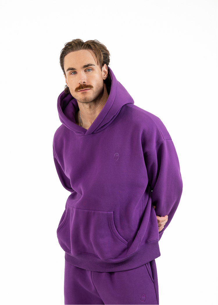A man modeling a matching purple hoodie and sweatpants set against a plain white background.