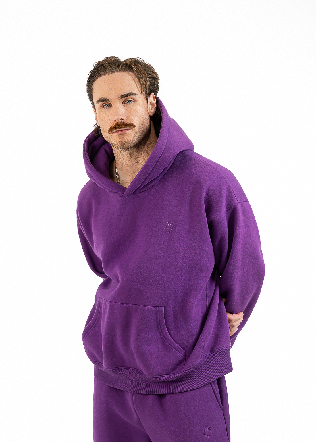 A man modeling a matching purple hoodie and sweatpants set against a plain white background.