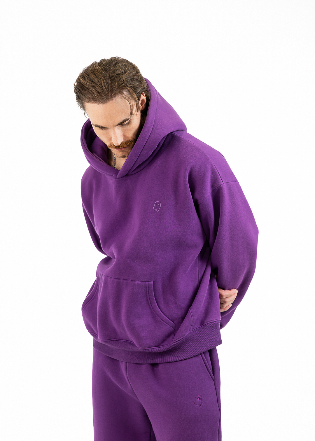 A man wearing a matching purple hoodie and sweatpants set, photographed against a plain white studio background.
