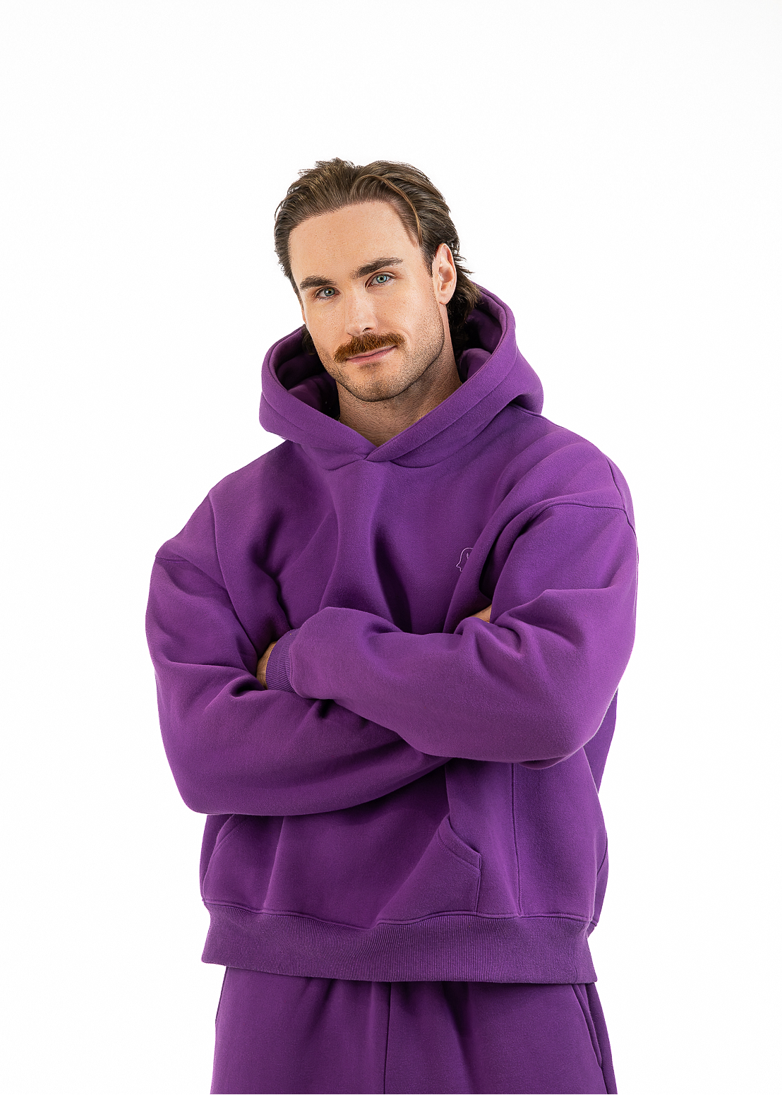 A man modeling a matching purple hoodie and sweatpants set against a solid white background.