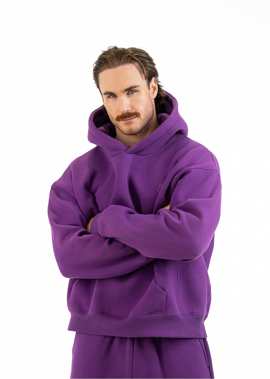 A man wearing a matching purple hoodie and sweatpants set, standing with arms crossed against a solid white background.