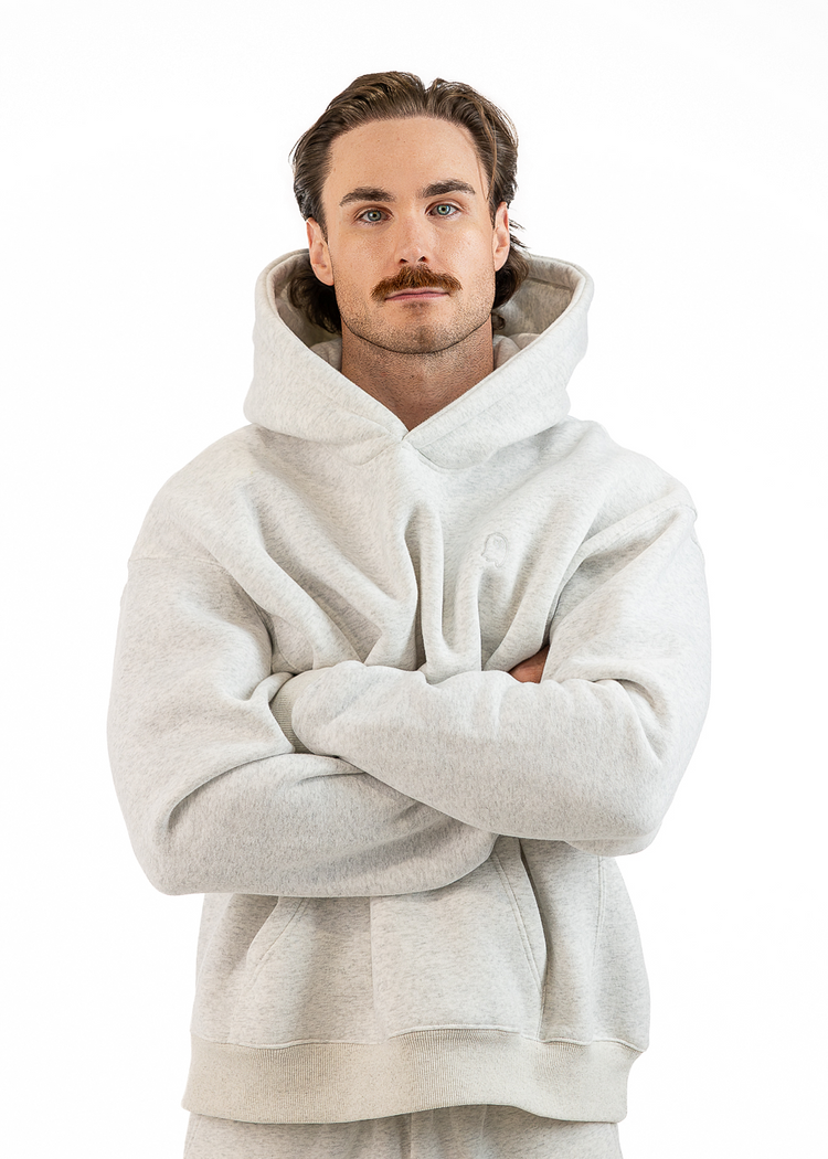 A man with a mustache wearing a light gray fleece hoodie and matching sweatpants, standing with arms crossed against a solid white background.